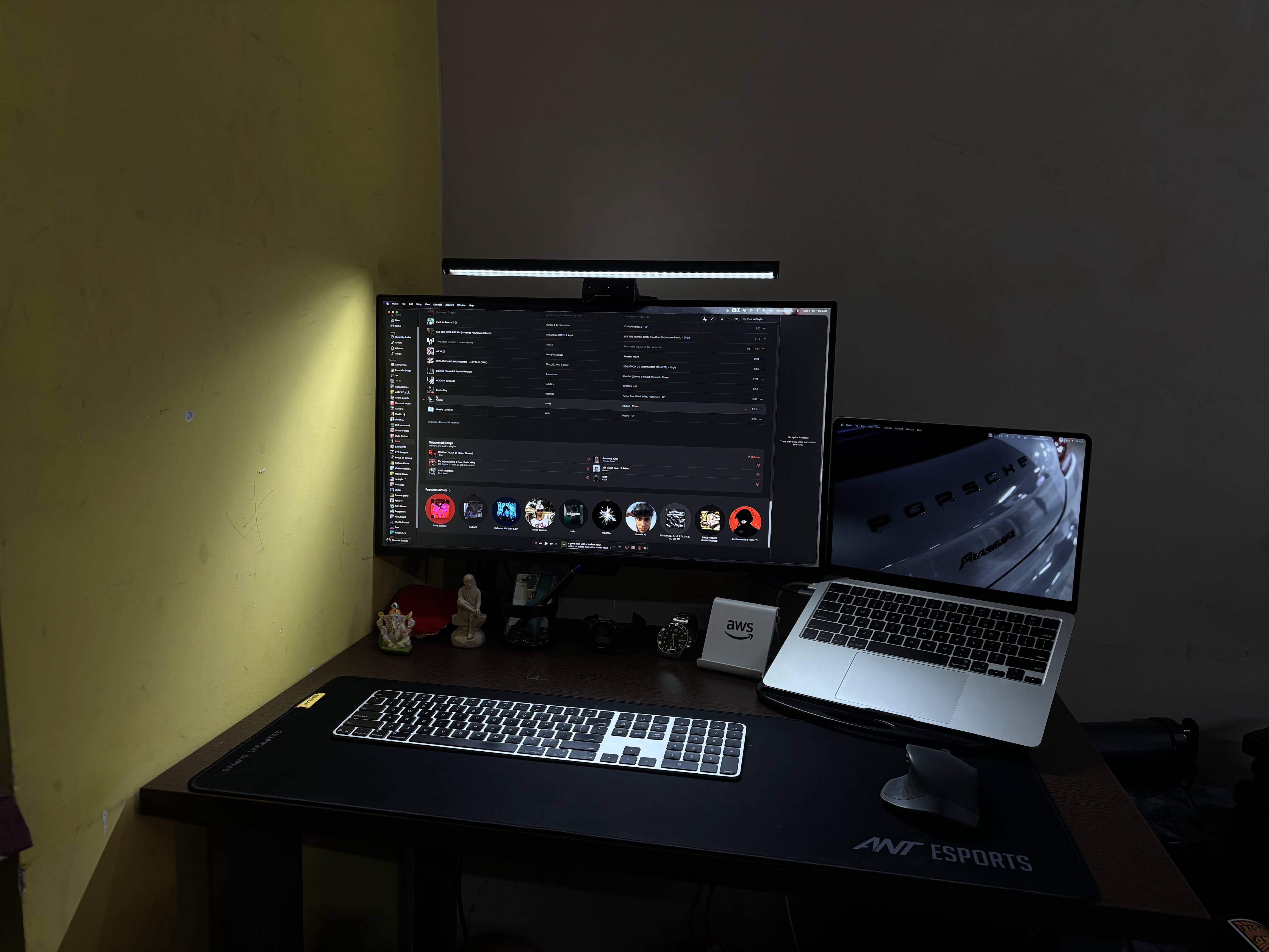 A dark desk setup with a monitor on an arm, a MacBook on a stand, a mechanical keyboard and mouse